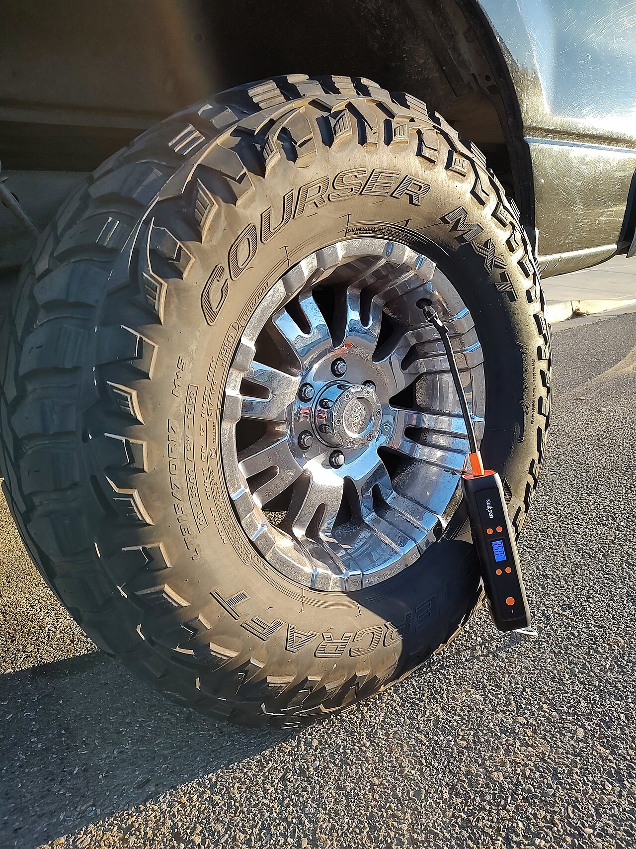 Truck tire being inflated with an air pump hose — a digital pressure gauge reads the pressure as the tire fills
