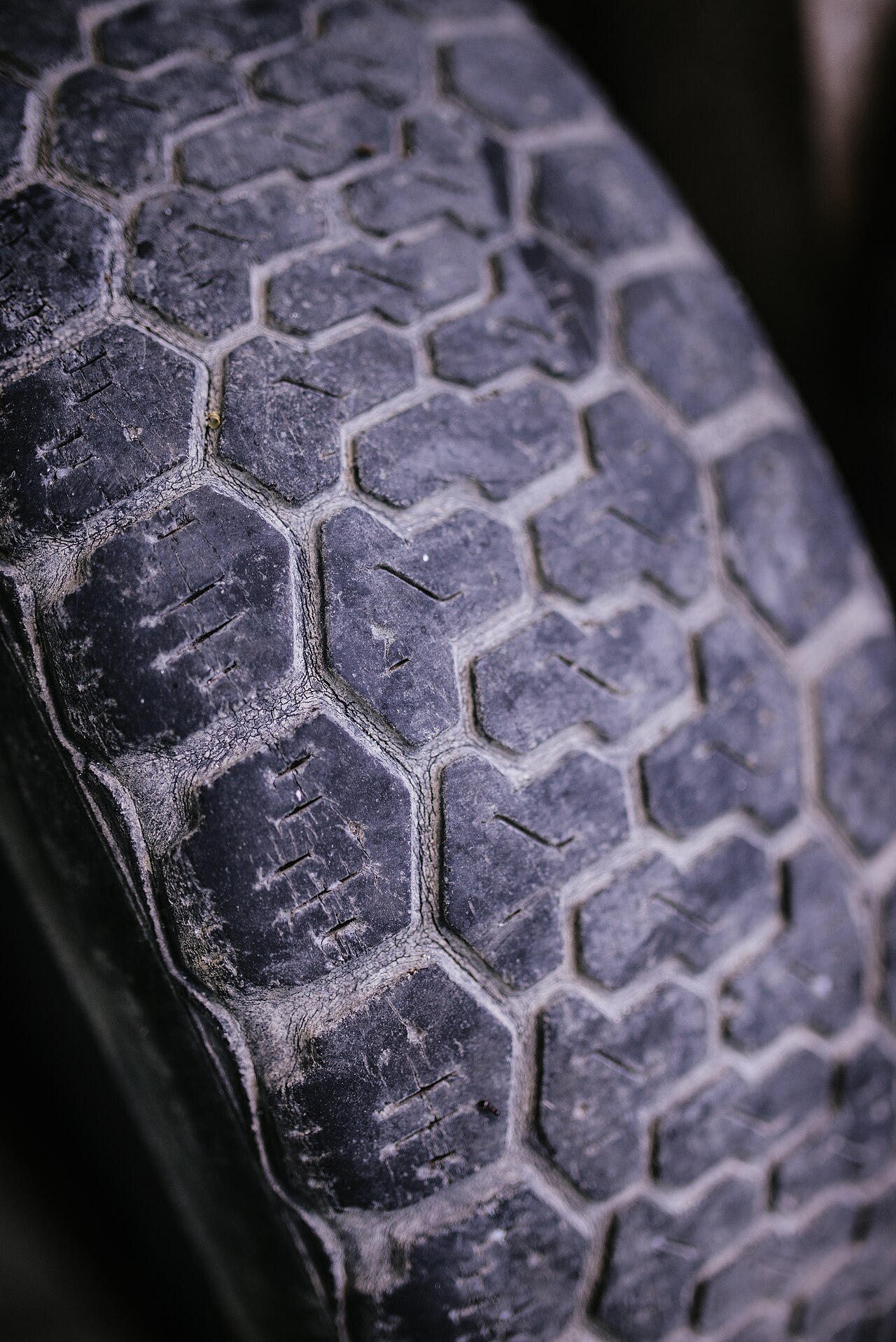 Close-up of an aged tire tread showing cracking between the tread blocks — the visible signs of rubber aging